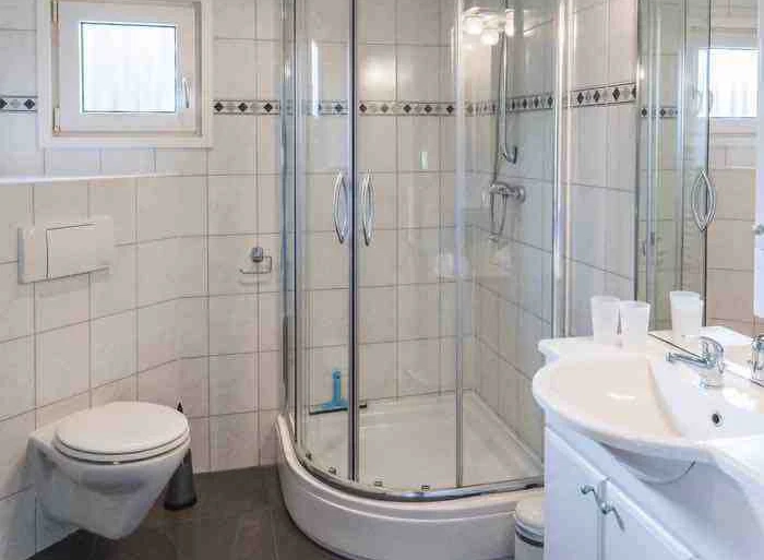 Badkamer met toilet, wastafel en douchecabine met glazen deuren en witte tegels.