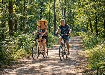 Familie fietst met kind in kinderzitje op bospad in de zomer.
