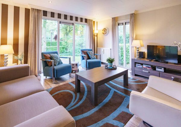 Gezellige woonkamer met blauwe fauteuils, bruine accenten en groot tapijt.