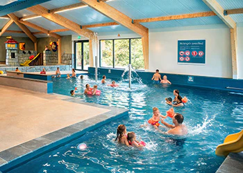 Indoor zwembad met spelende kinderen en volwassenen, fontein en glijbaan. Vakantiepark zwembad.