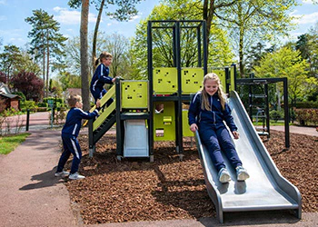 Kinderen spelen op een groene en grijze speeltoren met glijbaan in een park. Buitenspelen.