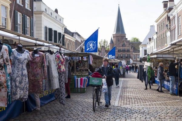 Markt in Nederland met man, fiets en kledingkramen. Kerk op de achtergrond.