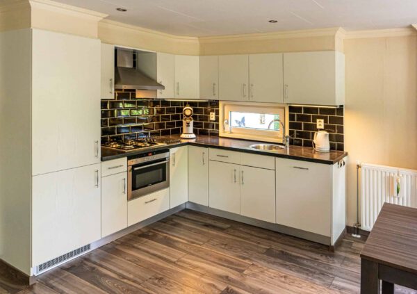 Moderne keuken met witte kasten, zwarte tegels en houten vloer.