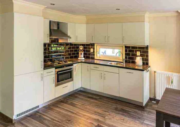 Moderne keuken met witte kasten, zwarte tegels en houten vloer.