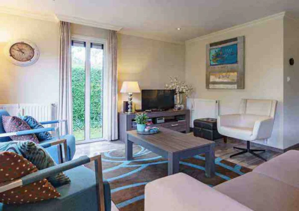 Woonkamer met blauwe stoelen, grijze tafel en tv. Modern interieur met kunst en natuurlijk licht.