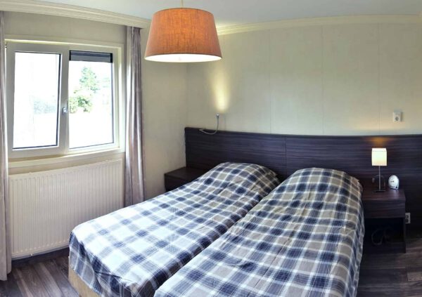 Slaapkamer met twee bedden, ruitjesdekbedden, nachtkastjes en raam met uitzicht.