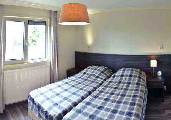 Slaapkamer met twee eenpersoonsbedden, ruitjesbeddengoed, nachtkastjes en raam met gordijnen.