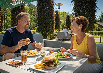 Lachend stel geniet van burgers en frietjes op terras in de buitenlucht.