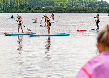 Mensen suppen op een meer op zonnige dag. Groene bomen op de achtergrond. Wateractiviteit in de natuur.