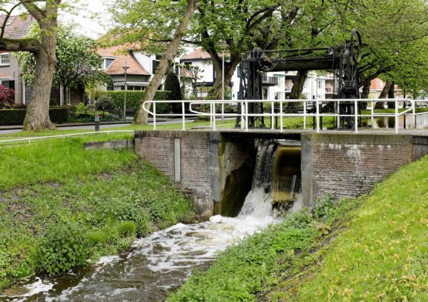 Watermolen in een pittoresk Nederlands dorp met een bakstenen brug en groene omgeving.